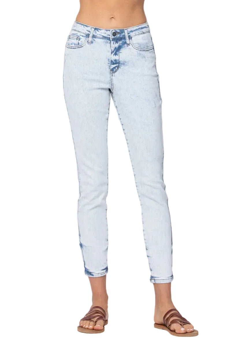 A person wearing light-wash blue skinny jeans with rolled cuffs and brown flat sandals, shown from the waist down against a plain light gray studio background.