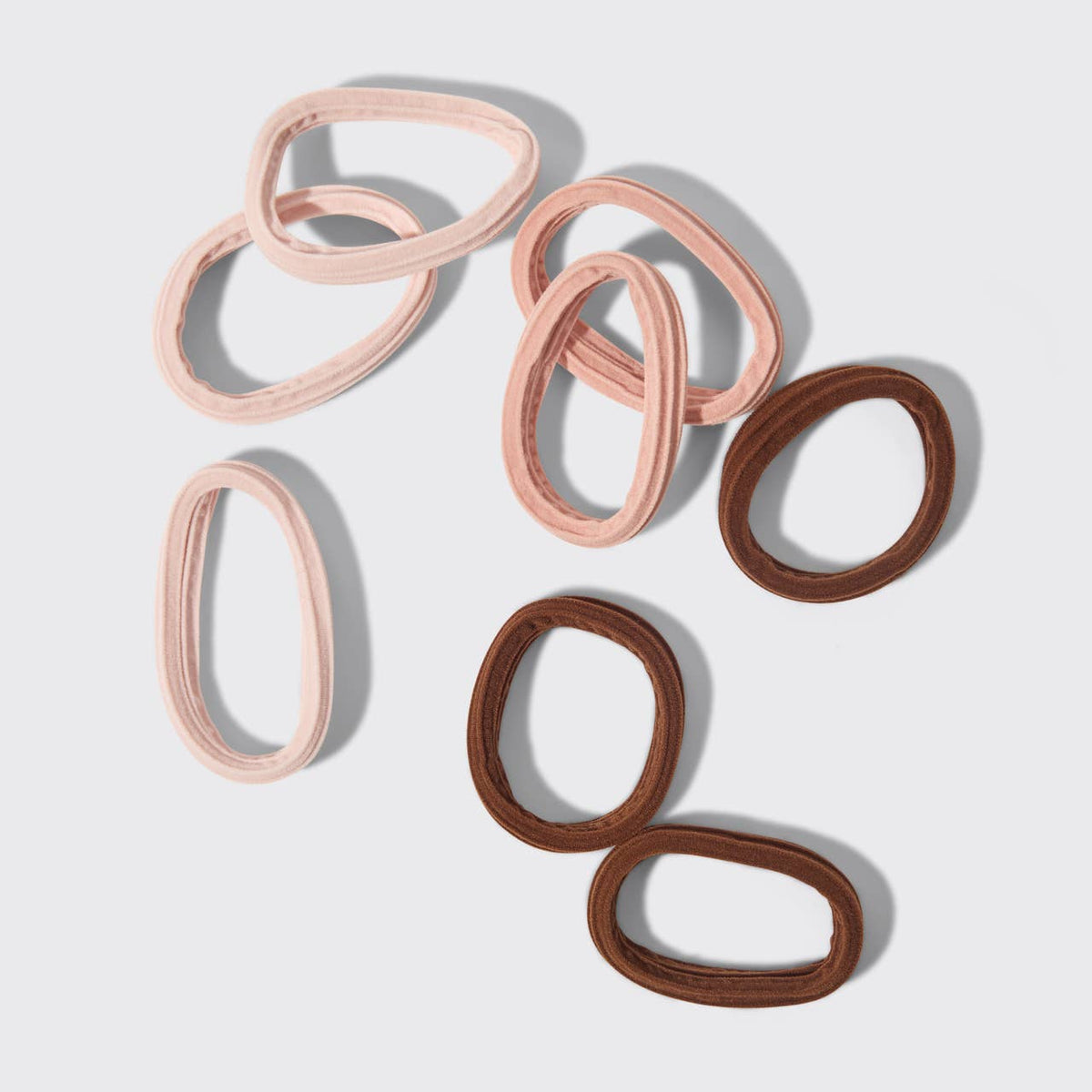 Eight KITSCH seamless hair elastics in blush pink and brown laid out on white