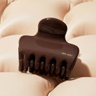 Chocolate brown KITSCH cloud claw clip resting on a cream puffy pillow