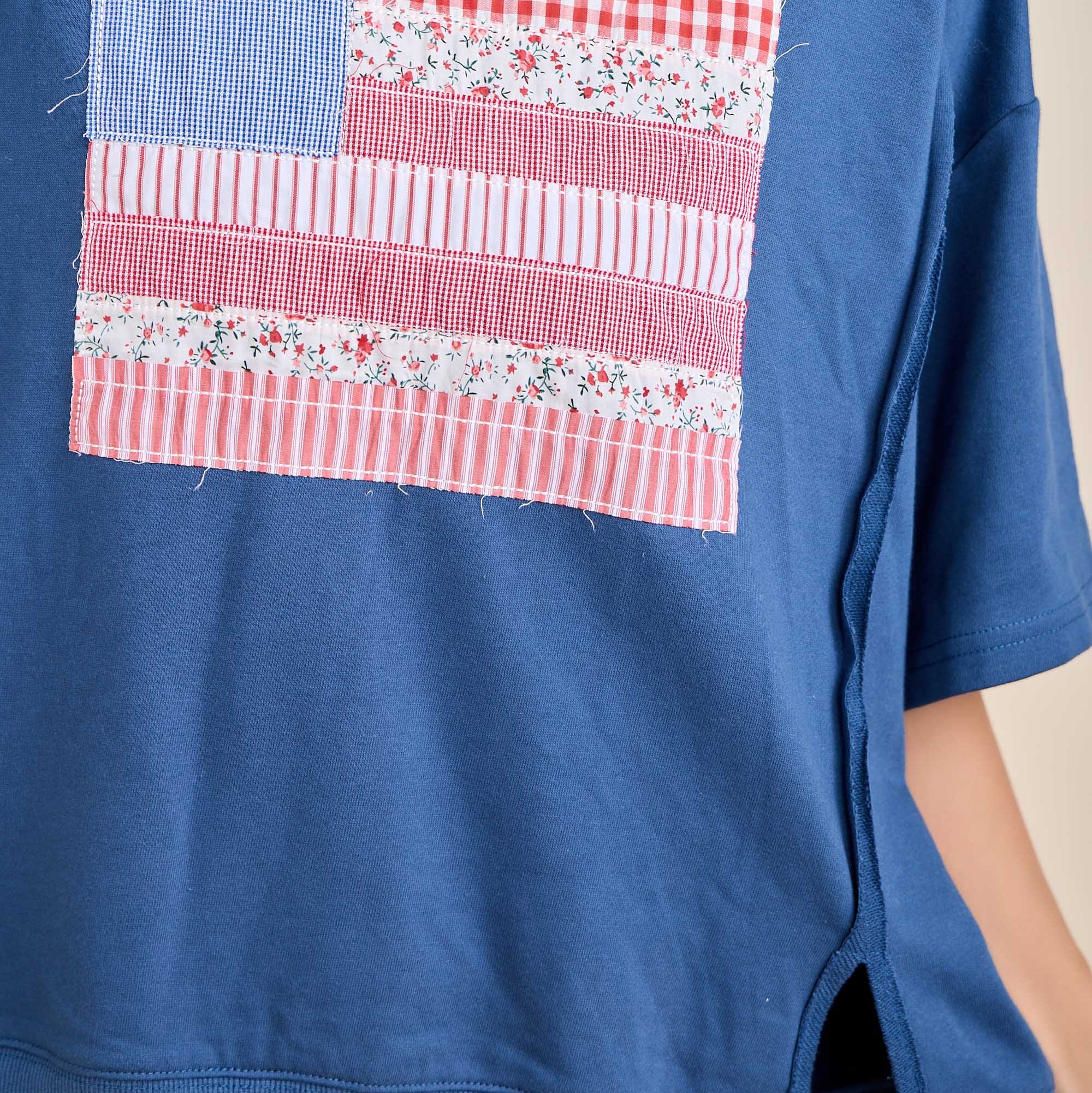 Blue sweatshirt with a patchwork design resembling an American flag on a neutral background