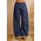 Close-up front view of navy wide leg pants with a tiny pink floral print and button front, worn with platform sandals