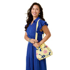 Woman in a blue dress holding a yellow floral handbag against a yellow background