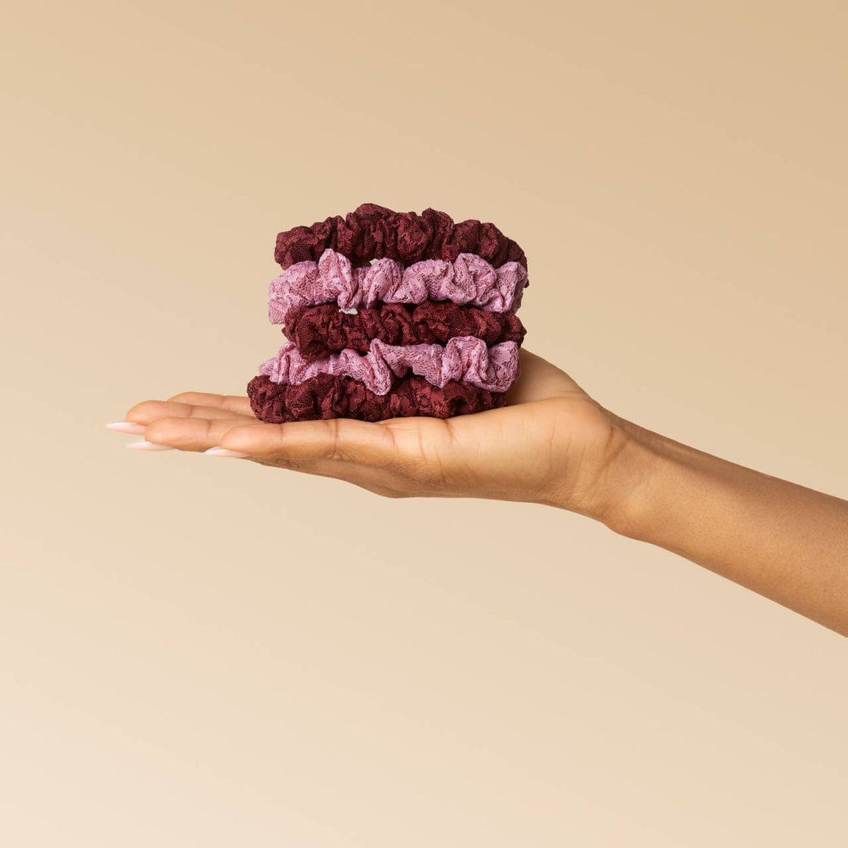 Hand holding a stack of burgundy and dusty pink KITSCH lace scrunchies