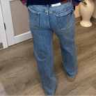  light blue jeans, standing in an indoor room with a pink wall and wood floor.