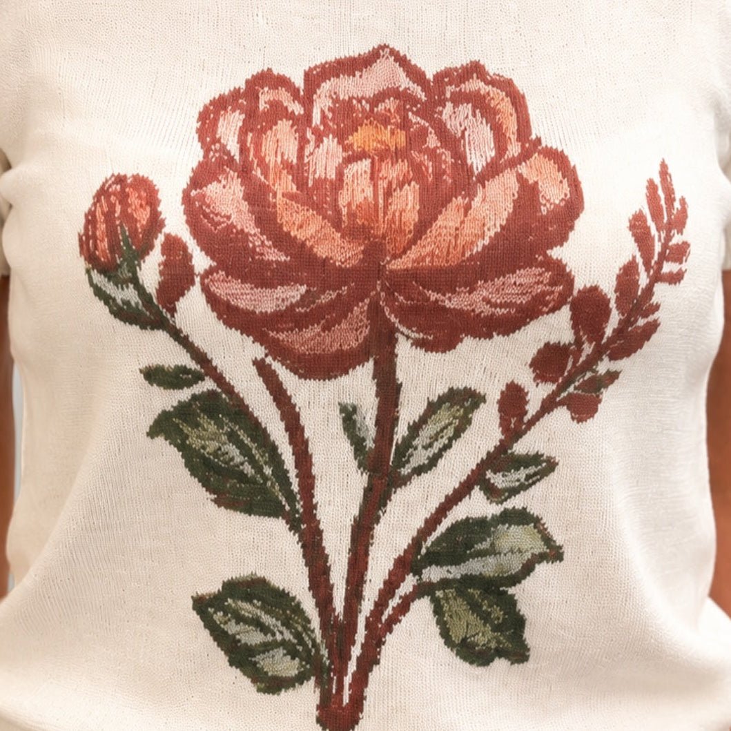  cream-colored short-sleeve knit top with a large embroidered rose design in red, pink, and green on the front