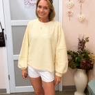 Woman wearing a light yellow sweatshirt and white shorts standing in a room with decorative elements.