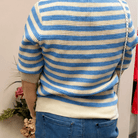 Person wearing a blue and white striped sweater and blue shorts, standing in a room with a neutral wall.