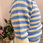Mannequin wearing a blue and white striped sweater with a blurred background of flowers.