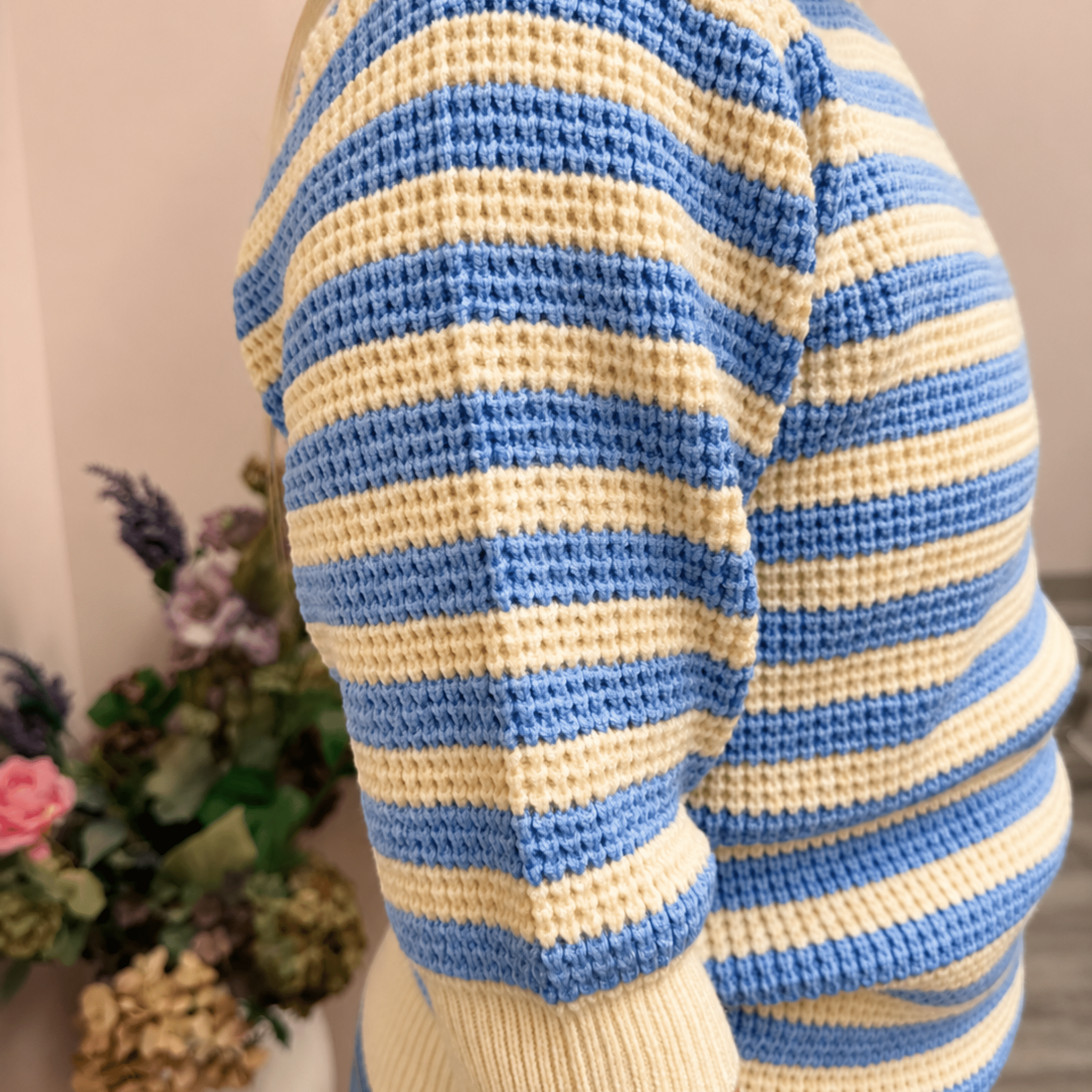 Mannequin wearing a blue and white striped sweater with a blurred background of flowers.