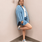 Woman wearing a blue denim jacket and shorts against a plain wall.