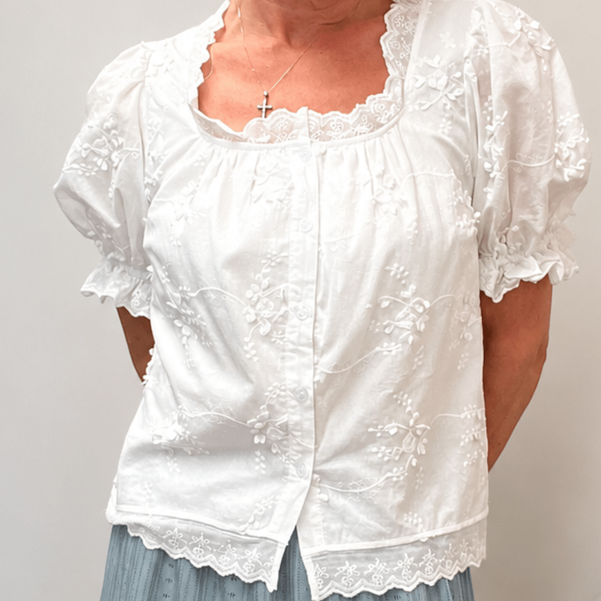 Woman wearing a white lace top and blue skirt with a neutral background