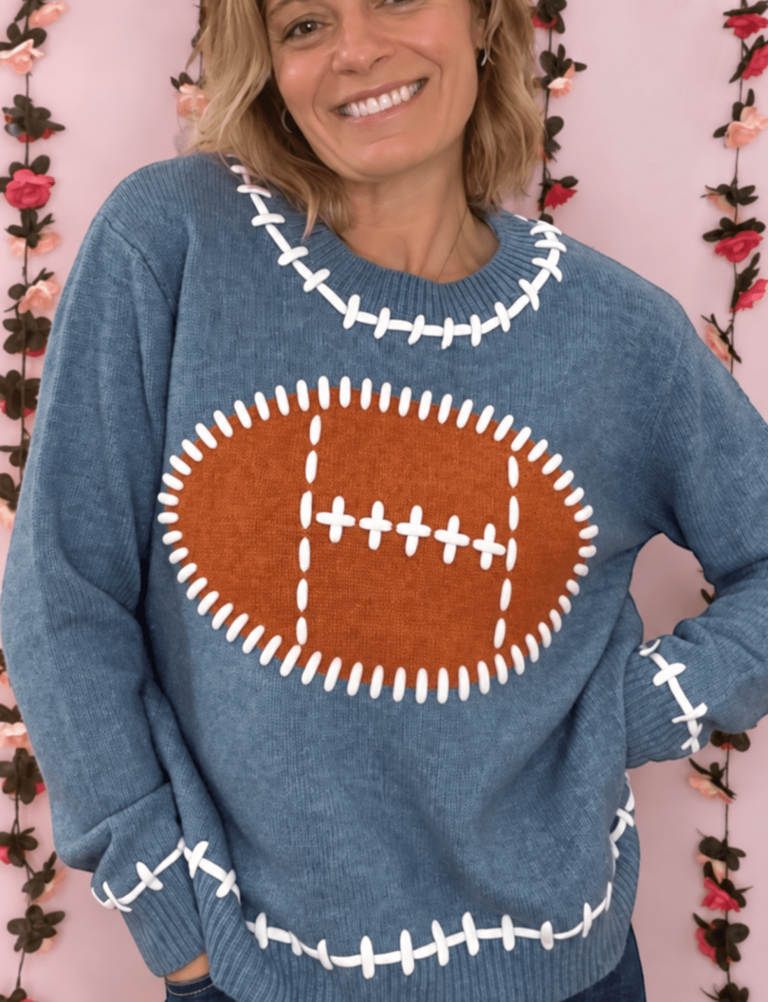 Woman wearing a dusty blue football knit sweater with a brown football graphic and white stitch details