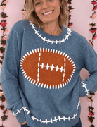 Woman wearing a dusty blue football knit sweater with a brown football graphic and white stitch details