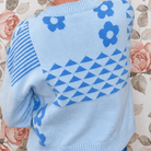 Close-up of light blue knit sweater back showing blue daisy, stripe and geometric triangle knit details