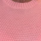 Close-up of a pink knit sweater showing the ribbed crew neck and textured knit pattern.