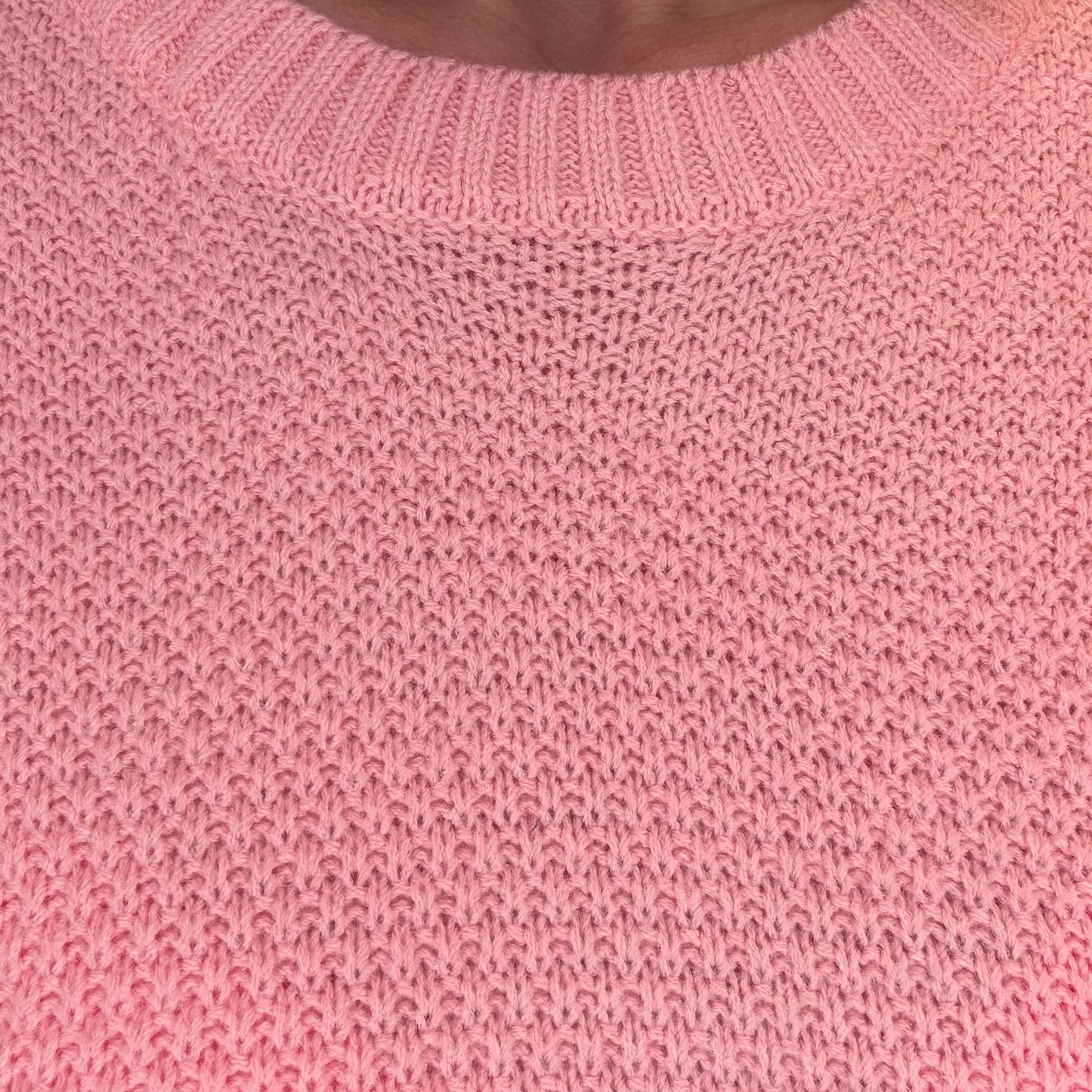 Close-up of a pink knit sweater showing the ribbed crew neck and textured knit pattern.