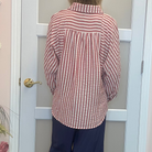 A person viewed from behind wearing a red and white vertically striped button-up shirt and navy wide-leg pants, standing in front of a white door in an indoor room.
