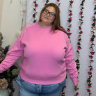 Front view of plus size model in a bubblegum pink crewneck sweatshirt with ribbed cuffs and hem, styled with jeans