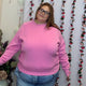 Front view of plus size model in a bubblegum pink crewneck sweatshirt with ribbed cuffs and hem, styled with jeans