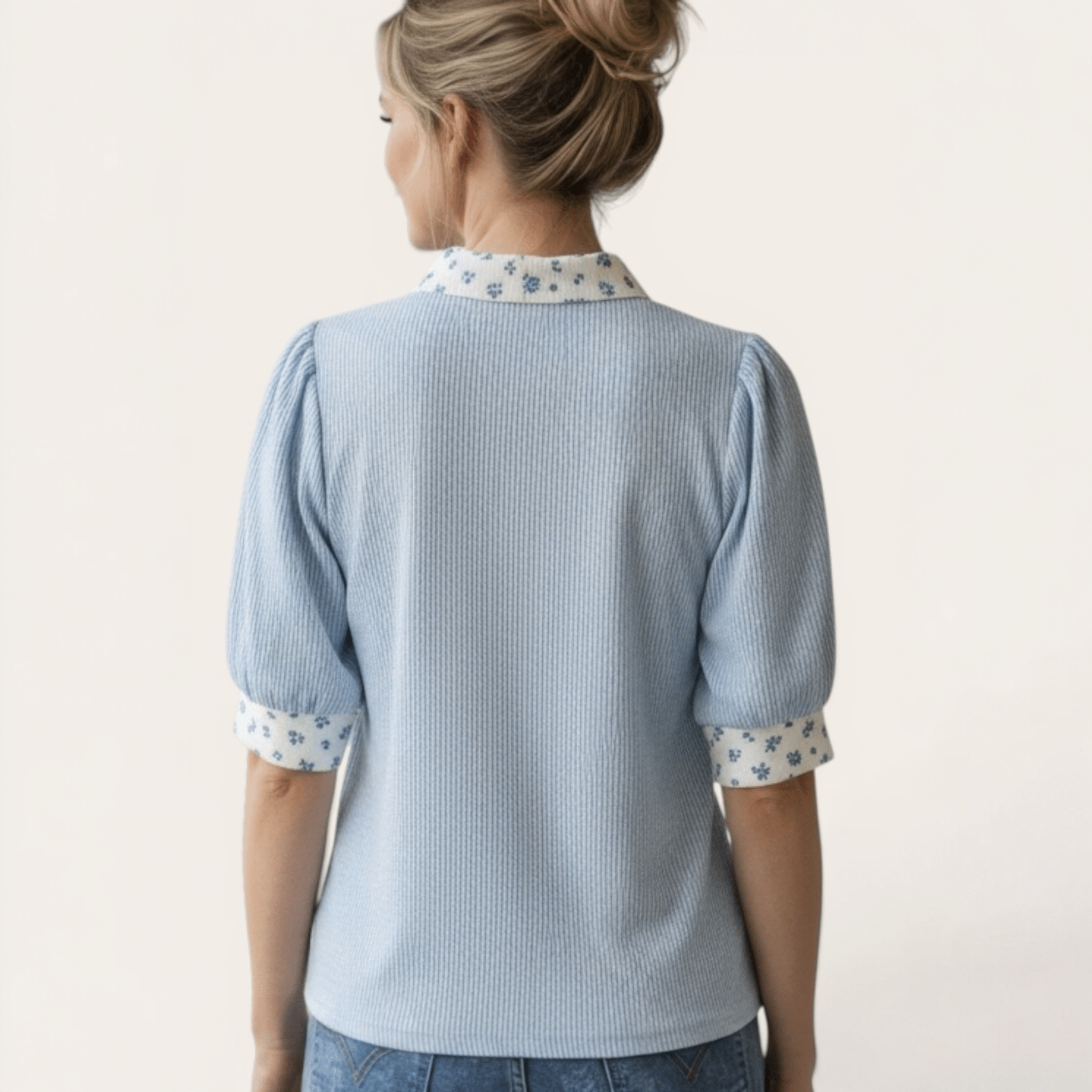 Woman wearing a light blue textured blouse with floral cuffs and collar on a white background