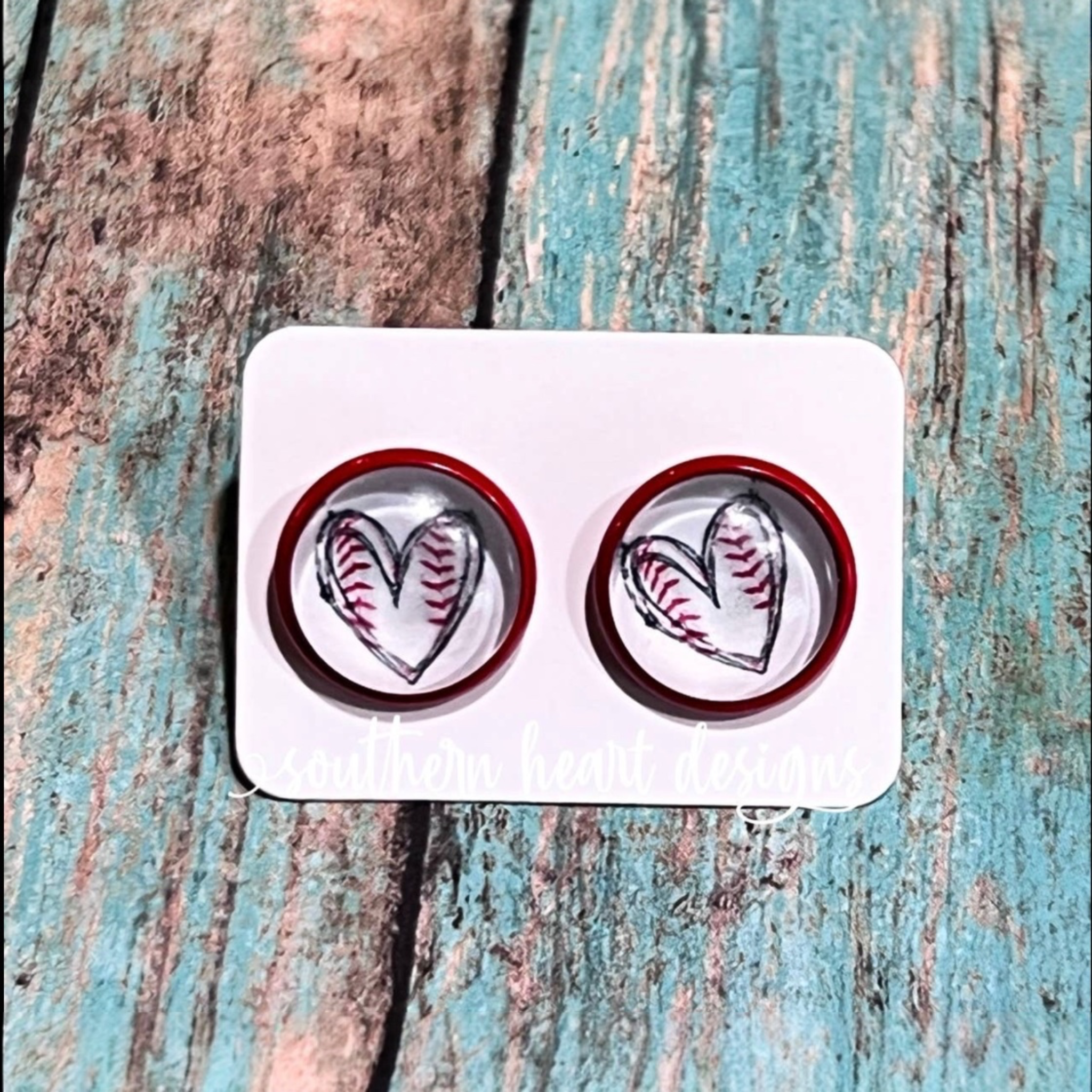 Heart-shaped  inside a circle shape earrings with red borders on a white card against a textured wooden background