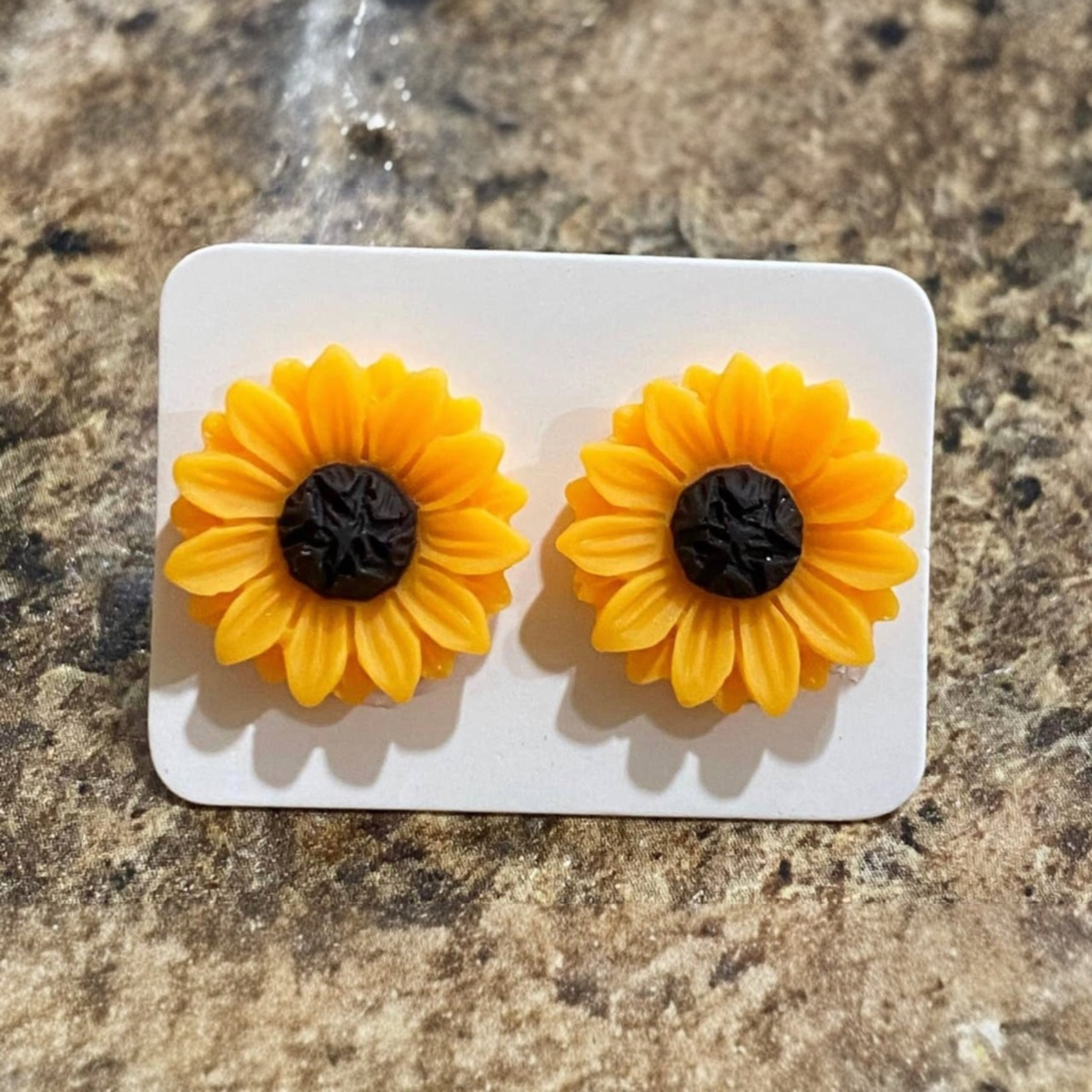 Sunflower-shaped earrings on a white card with a brown surface background