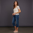 Woman wearing a white lace top and blue jeans against a dark background