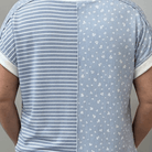 Person wearing a blue and white striped shirt with a patterned back, standing in front of a gray door.