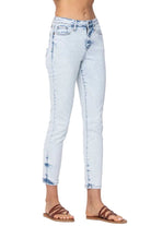 A person wearing light-wash blue cropped skinny jeans with faded detailing and brown strappy sandals, shown from the waist down against a plain light background.
