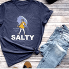 salty salt girl on a navy tshirt.  shown with denim pants on.a wooden background
