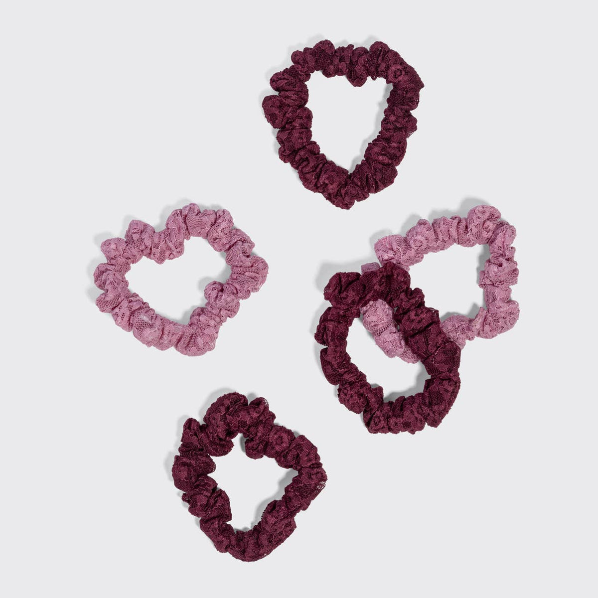 Five burgundy and dusty pink ruched lace scrunchies laid out on white