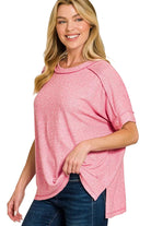 Woman wearing a candy pink melange tee with folded short sleeves, exposed seams and side slits, paired with dark jeans