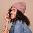 Smiling woman with curly hair wearing a blush pink KITSCH beanie and a denim jacket