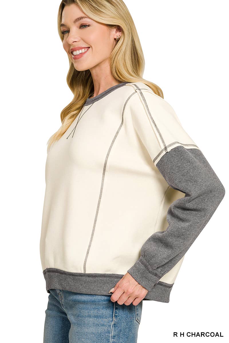 Side view of a cream and charcoal color block fleece sweatshirt showing the relaxed oversized fit and exposed seam details