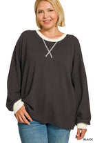 Woman wearing a plus size black raised rib pullover with cream contrast trim at the neck and cuffs and a V-stitch neckline, styled with light wash jeans