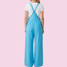 Person wearing a blue jumpsuit with a white shirt on a pink background