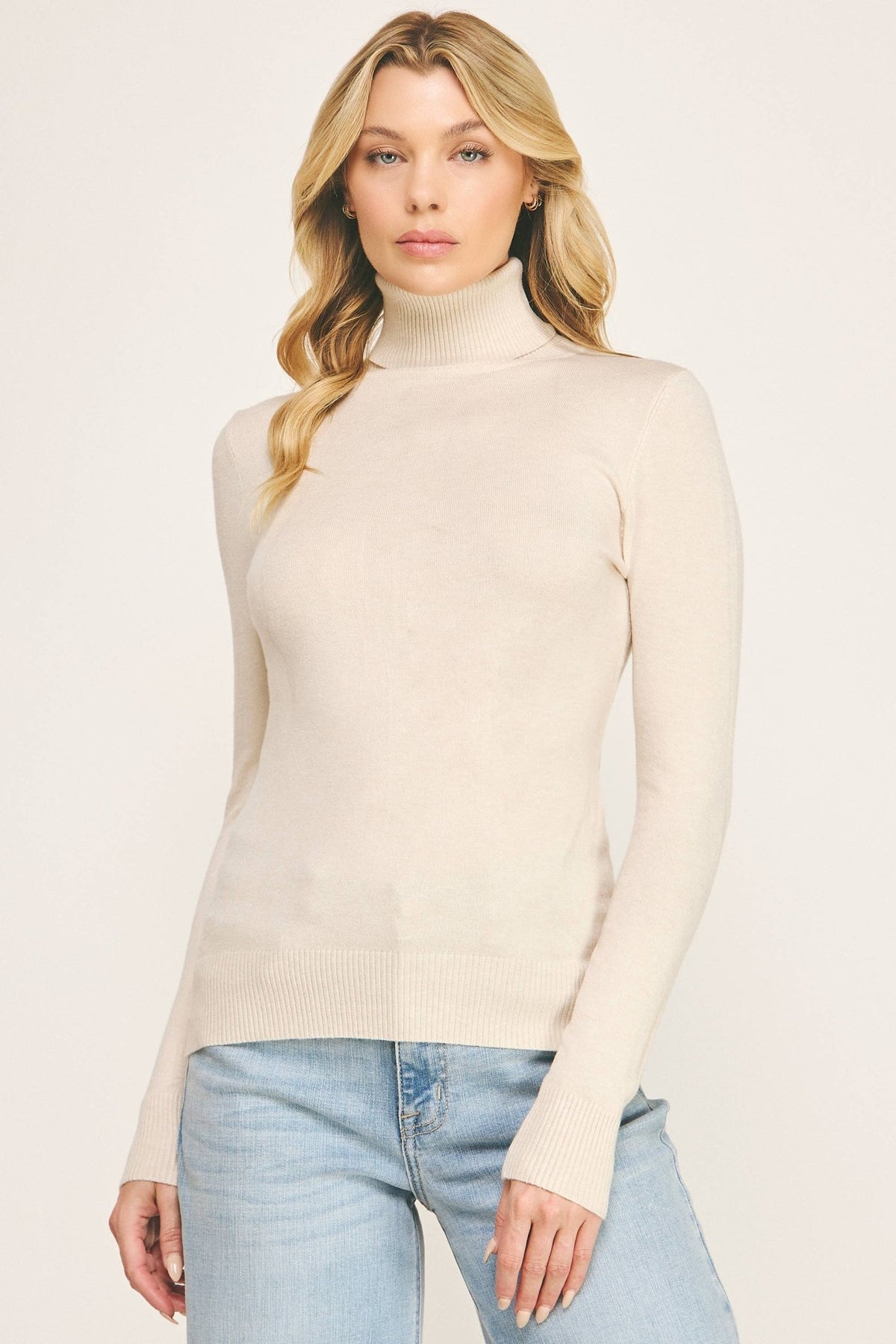 Woman wearing a beige fitted turtleneck sweater tucked into light-wash jeans