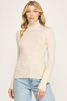 Woman wearing a beige fitted turtleneck sweater tucked into light-wash jeans