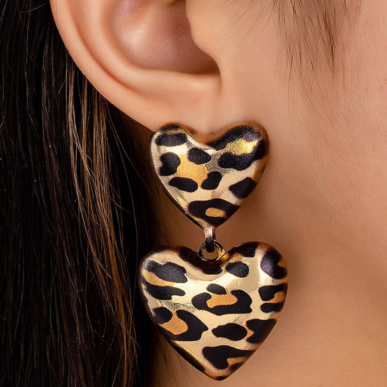 Leopard print heart-shaped earrings worn by a person.
