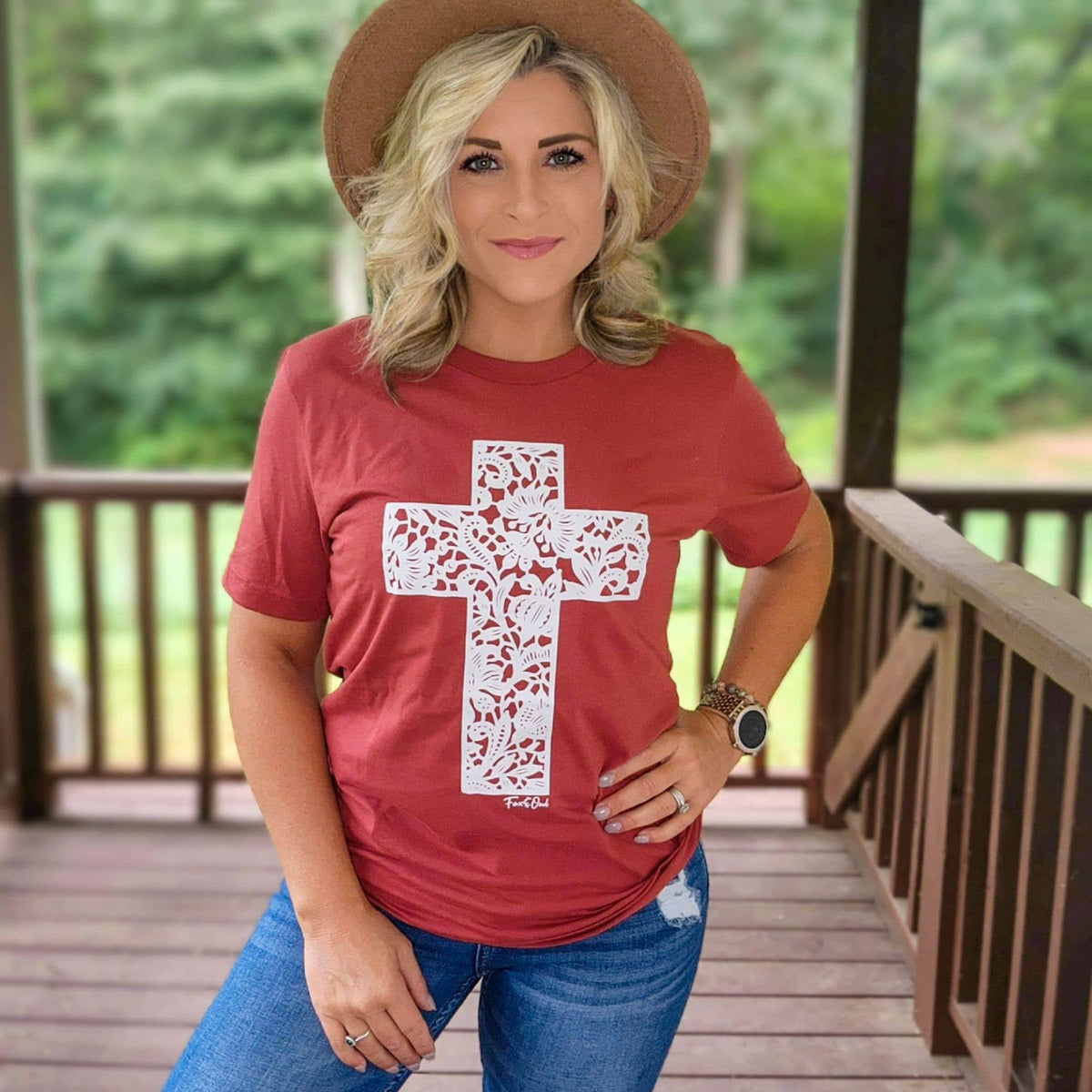 Woman wearing a rust lace cross Christian graphic tee with jeans and a felt hat