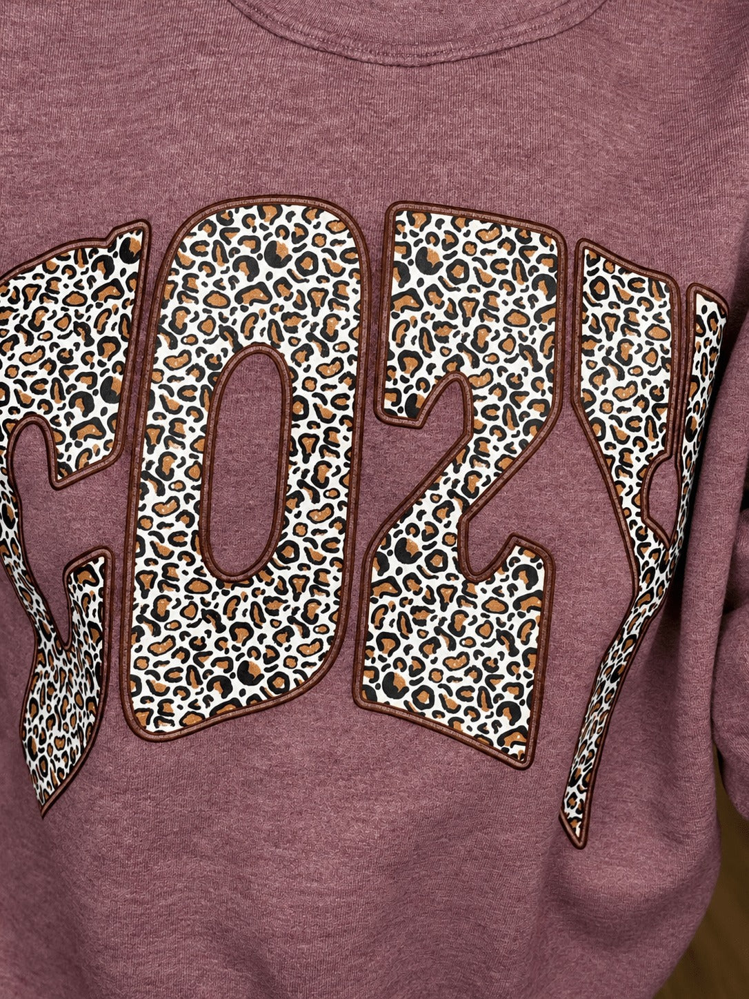 Close-up of the leopard print COZY graphic on the heather maroon sweatshirt