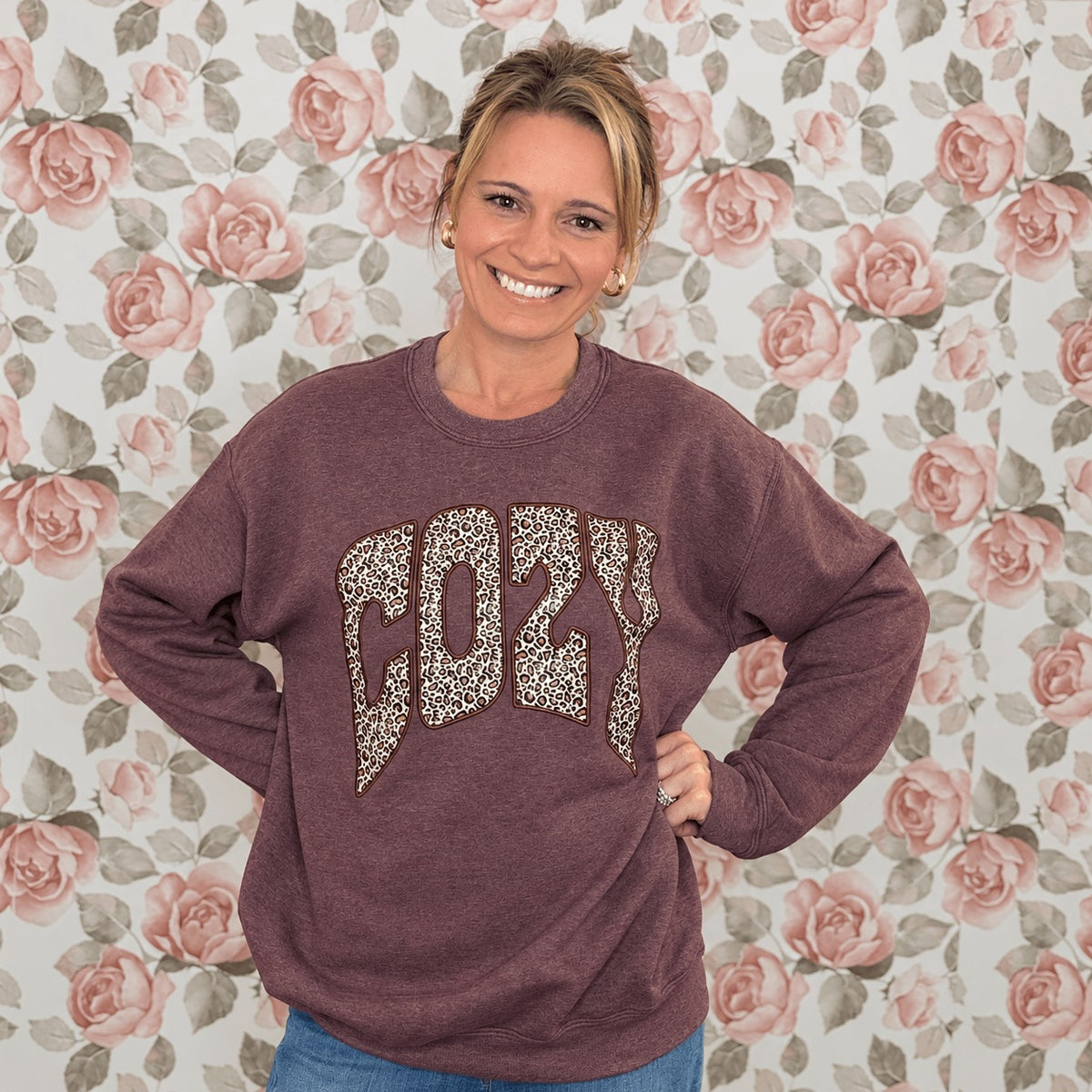 Woman wearing the heather maroon Leopard Cozy crewneck sweatshirt with a leopard print COZY graphic