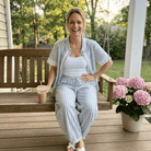 Woman sitting on a wooden swing with a drink, surrounded by flowers on a porch.