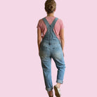 Person wearing blue denim overalls and a pink shirt on a pink background