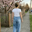 Back view of woman in Judy Blue High Waist Palazzo Featherweight Drawcord Jeans, fence and cherry trees in background