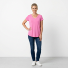 Woman wearing a pink t-shirt and blue jeans standing against a white background