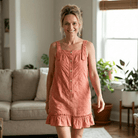 Woman wearing a orange coloredndress standing in a living room with plants and a couch.