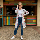 Woman wearing a floral cardigan, white shirt, and blue jeans standing in front of a colorful wooden wall.