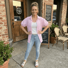 Woman in pink shirt and blue jeans standing outside a coffee shop.