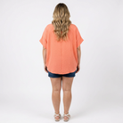 woman wearing a coral top with denim shorts facing a white background
